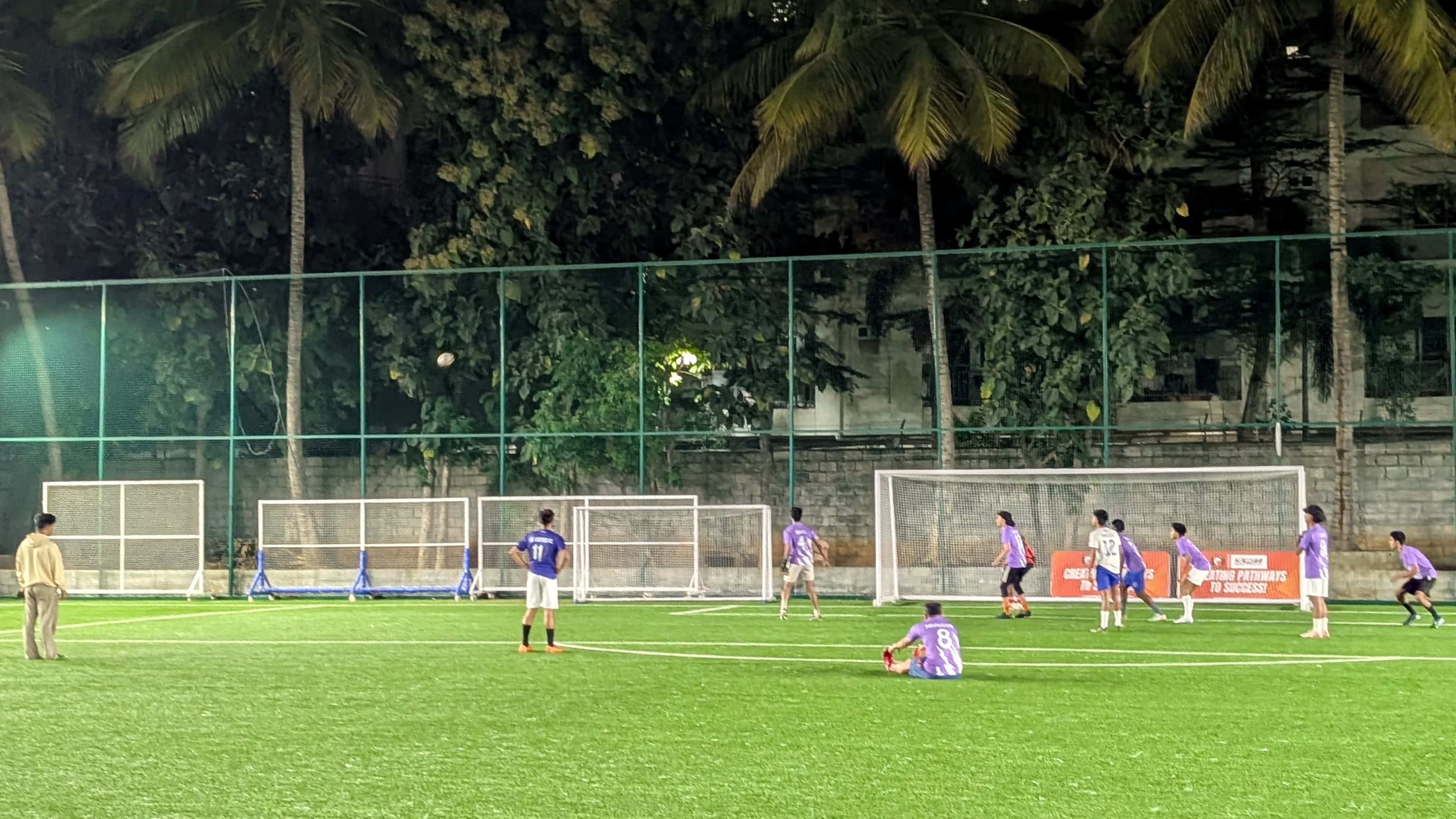 Two teams playing a 5-a-side football match on a floodlit turf at 3lok Football Fitness Hub, Bengaluru